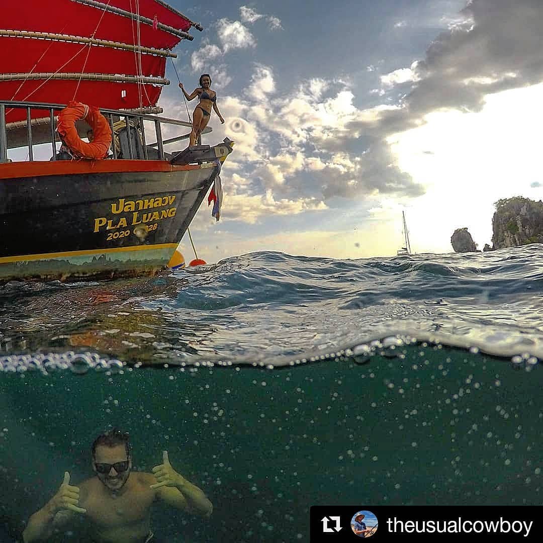 regram instagram photo by the usual cowboy of a man underwater smiling at the camera and a woman above water on a boat with a red sail