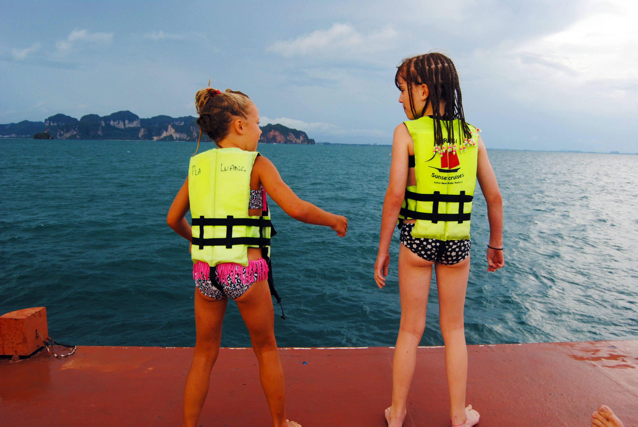 2 young girls ready to jump of the deck of a boat with krabi in the distance
