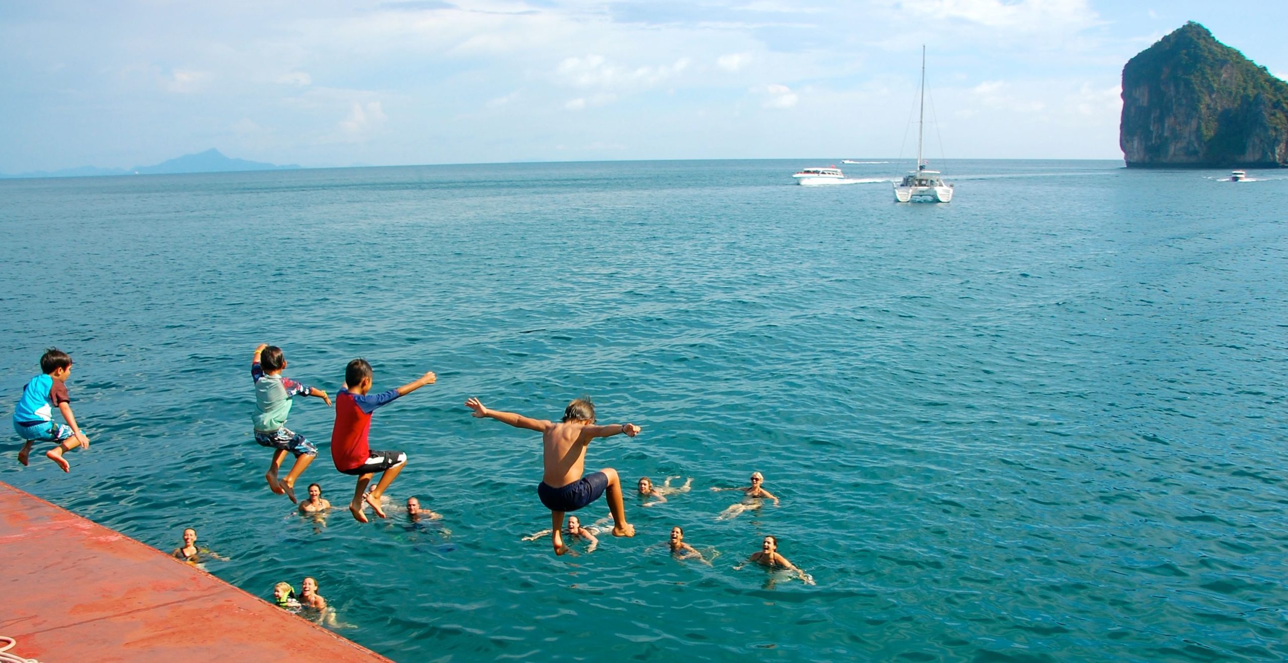 Kids jumping from the deck of a Krabi Morning Cruise with their parents in the water