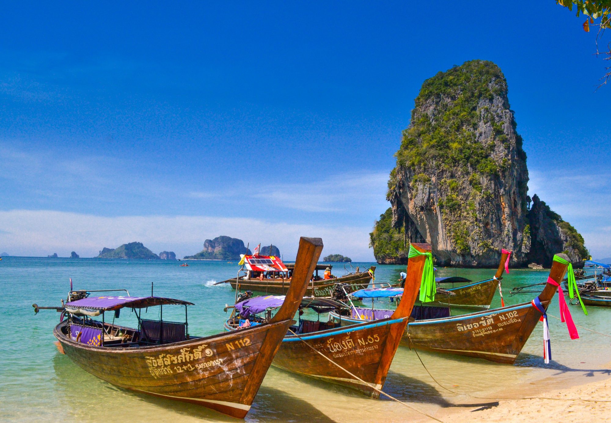 colourful longtail boats on the beach in railay with the islands in the background