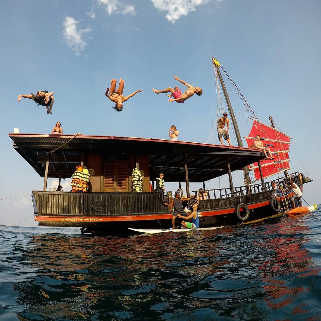 Thailand booze cruises - people doing backflips off Krabi Sunset Cruise pirate ship boat top deck, with two people on a paddleboard in front of it