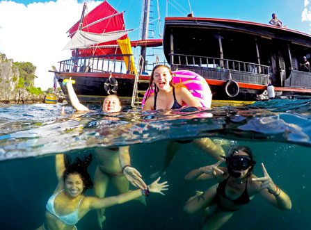 Guest posing in rubber ring, and others posing under water in front of boat during a Krabi Private Morning Cruise with blue skies and island in the background