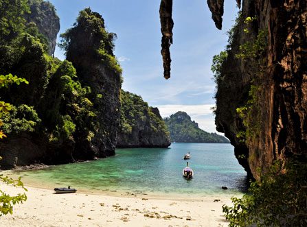 Image of boats at Railay Beach in Krabi, Thailand showing clear water, white sand and surrounded by rocky cliffs