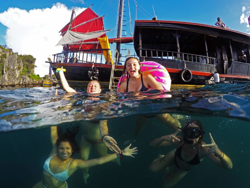 4 girls snorkelling and swimming with half the photo showing underwater scenes and the above showing a pirate boat in the background