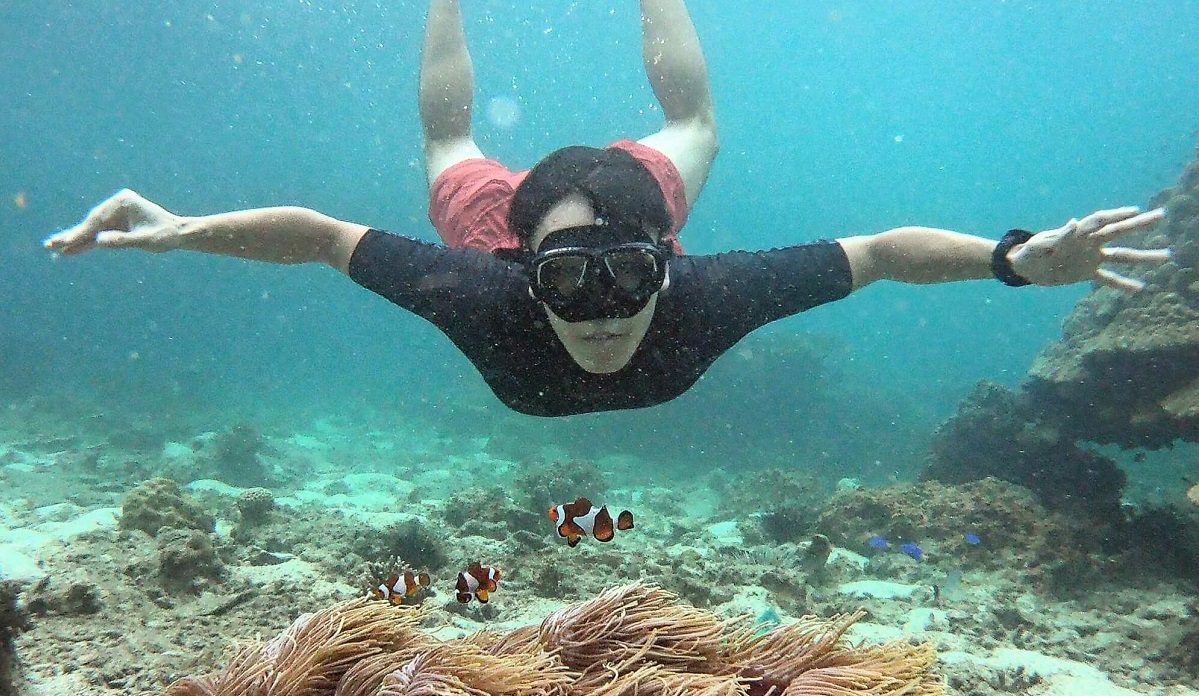 a man swimming underwater with a snorkel mask facing the camera with a clown fish in front of him during a krabi boat tour