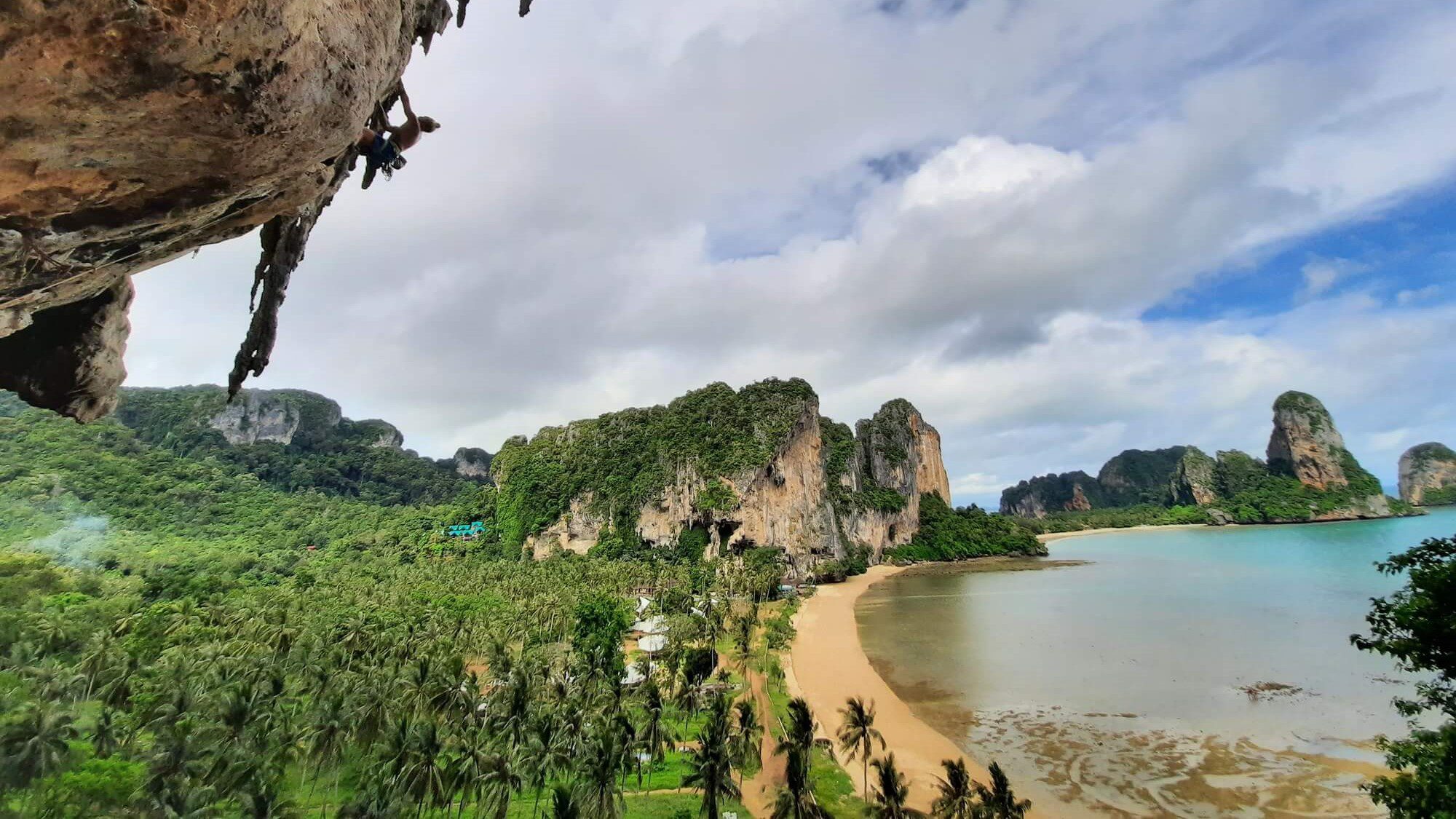 a climber on a high overhang cliff with views across railay krabi in the background