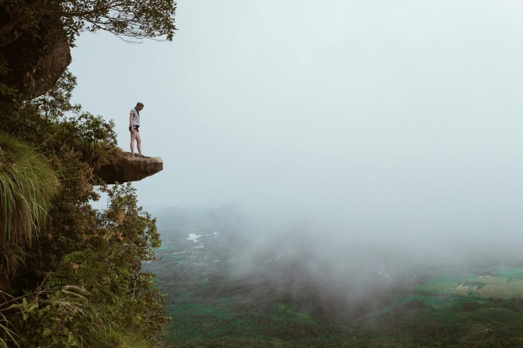 A person standing on a jutting rock, overlooking the Dragon Crest Mountain Hike: Khao Ngon Nak Viewpoint with a misty background