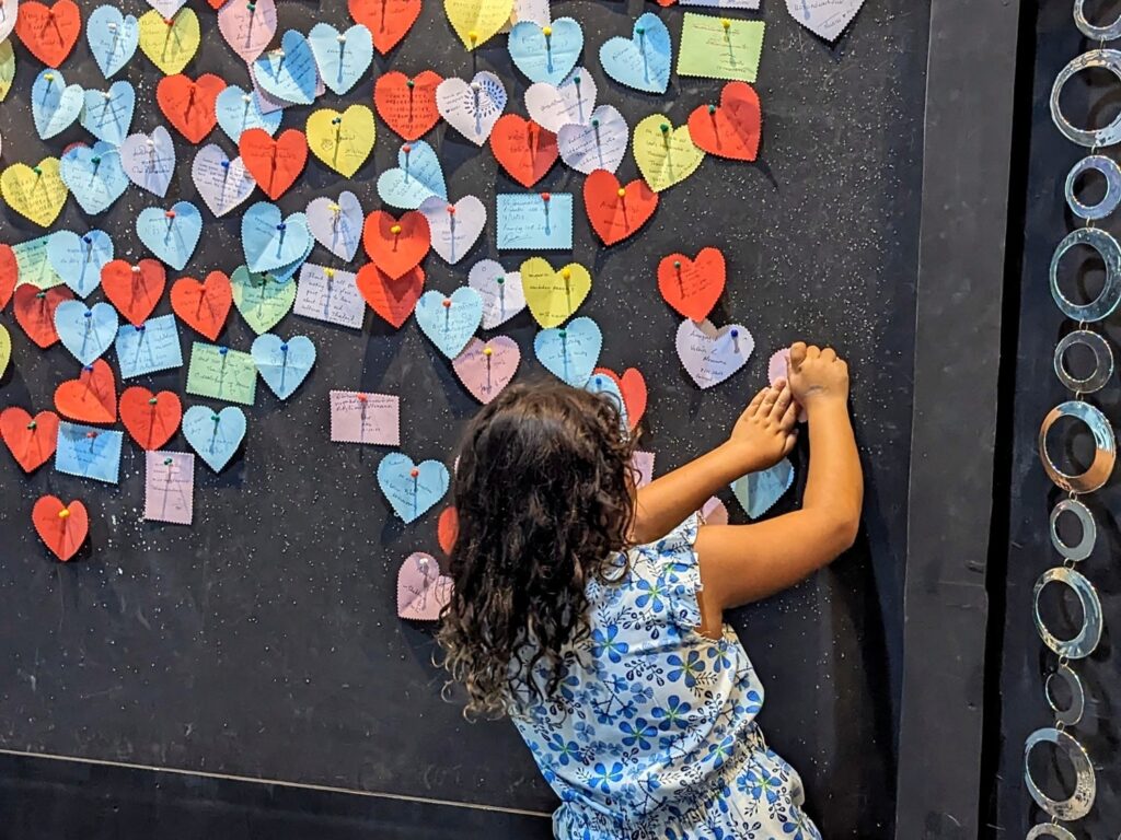 child pining a paper heart to a wall