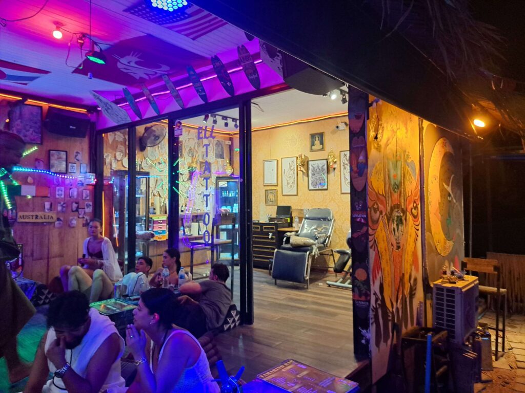 looking inside a tattoo shop in railay, krabi. the door is open and there are bar guests sitting outside