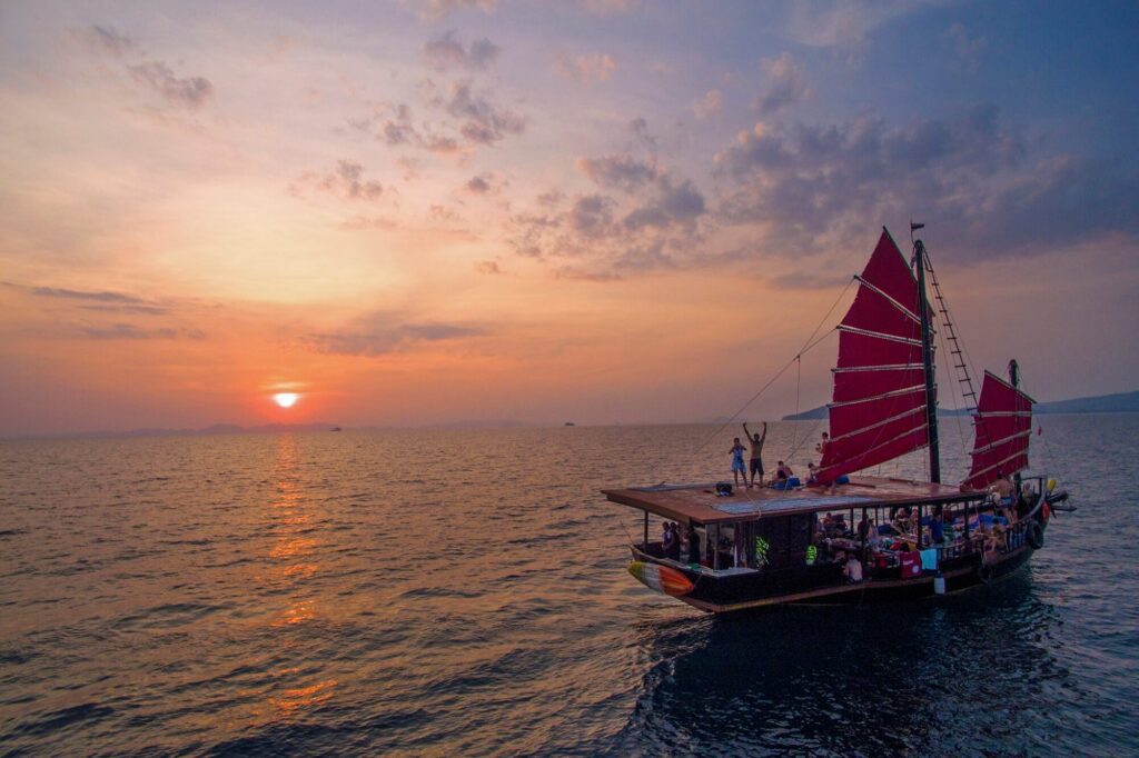 a traditional junk boat on the seas with its red sails up a sunset