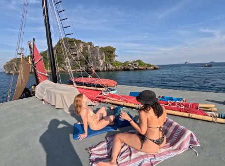 Two women relaxing on the deck of a Thai junk boat with limestone islands in the background