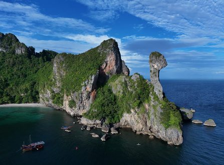 Aerial view of Chicken Island in Krabi with limestone cliffs, lush jungle, and a red-sailed junk boat below