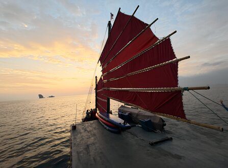Voile rouge d'une jonque traditionnelle avec un ciel de coucher de soleil pastel et une mer calme en arrière-plan.