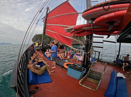 Les invités se détendent sur des coussins à côté de la voile rouge à l'avant du bateau.