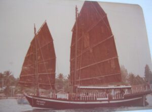 Foto antigua del Pla Luang con velas rojas gemelas atracado cerca de palmeras