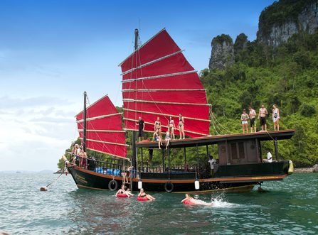 Guests jumping and swimming off a traditional red-sailed junk boat near Chicken Island