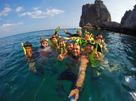 Group of snorkelers smiling and posing for a selfie in the sea with rocky cliffs in the background