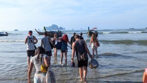 group of people wading into the water to a longtail boat in krabi