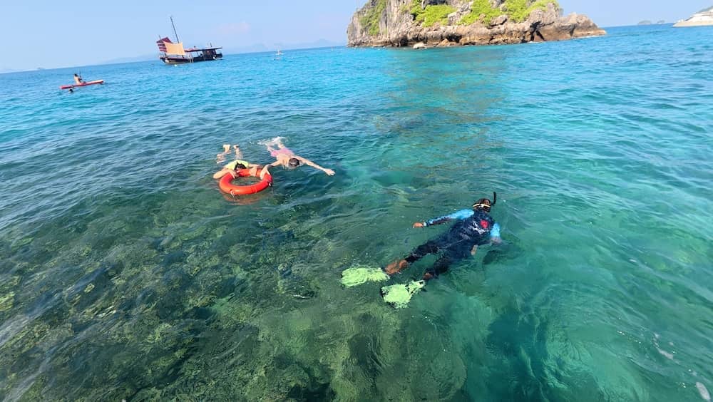 A guide taking 2 people around the reefs of Koh Ya Wa Sam on a life ring. Krabi Sunset Cruises junk boat in the background.