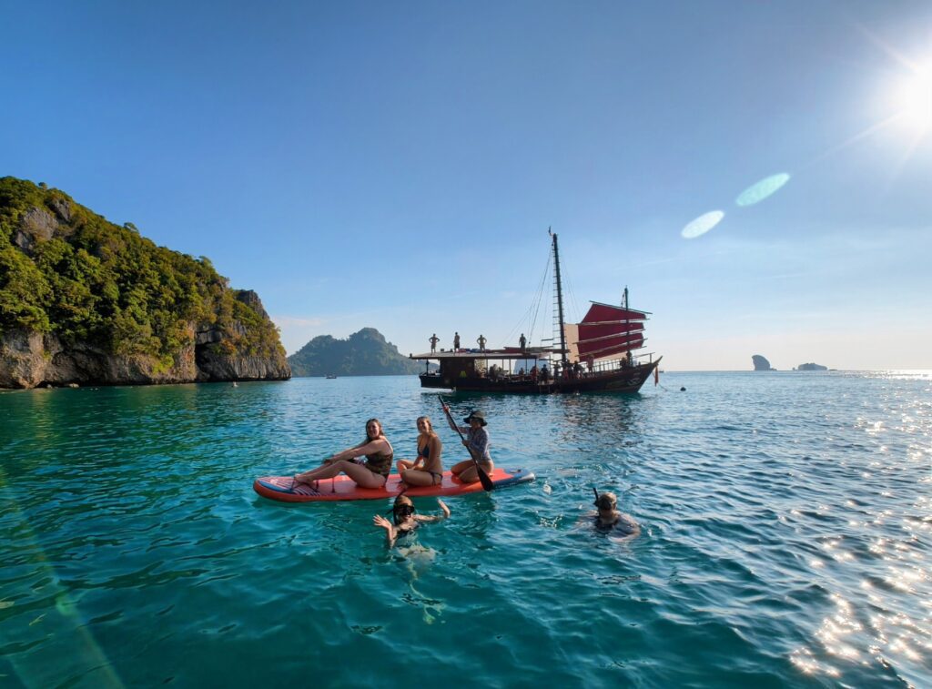 a group of contiki tour paddle boarders in the sea in krabi with a pirate boat and islands in the background