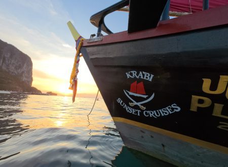 Primer plano del logotipo de Krabi Sunset Cruises en la proa del barco con una puesta de sol dorada reflejándose en el mar.
